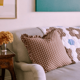 Trudie Constance Chocolate Ruffled Throw Pillow styled on a sofa with quilt
