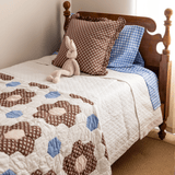 Trudie Constance Chocolate Ruffled Throw Pillow styled on a bed with a quilt