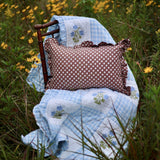Trudie Dorothy Blue Embroidered Quilted Throw Blanket styled in chair with throw pillow